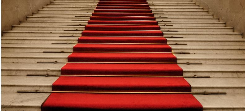 Breite Treppe mit rotem Teppich in der Mitte, beidseitig helle Stufen mit Metallleisten