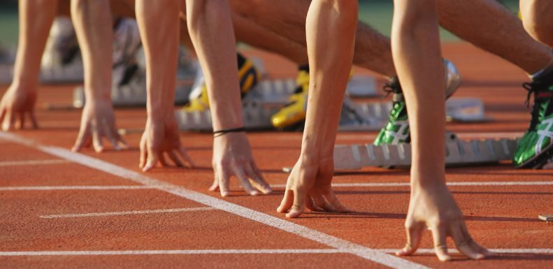 Mehrere Personen in Startposition auf Laufbahn, Hände an Startlinie, Startblöcke im Hintergrund