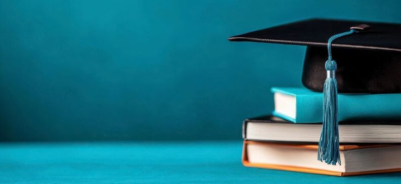 Abschlusskappe mit Quaste auf Stapel Bücher vor blauem Hintergrund