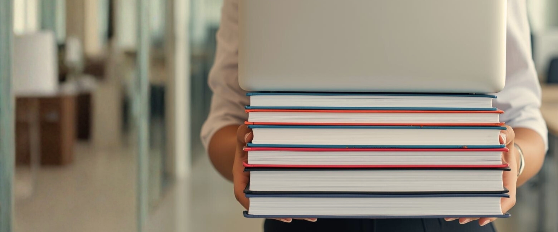 Person hält Stapel Bücher mit Laptop oben darauf in Innenraum